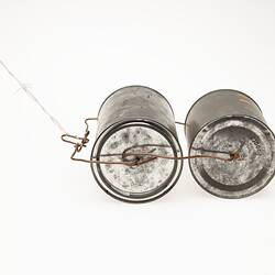 Two metal tins with lids. Bound together with wire. Cord at one end to pull them along. End view.