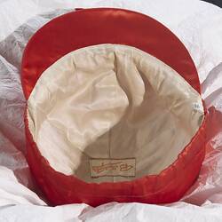 White fabric lining inside of red jockey cap. White label, yellow lettering.