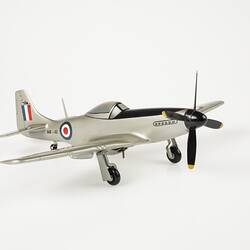 Wood model plane painted silver. Blue, white, red roundel on sides and wings. Red, white, blue flag on tail. Front black four blade propeller. Three wheels.