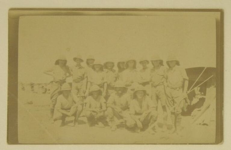 Posed group of unnarmed soldiers, tents pitched behind them.