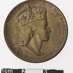 Round bronze medal with profile of a crowned woman, text surrounding.