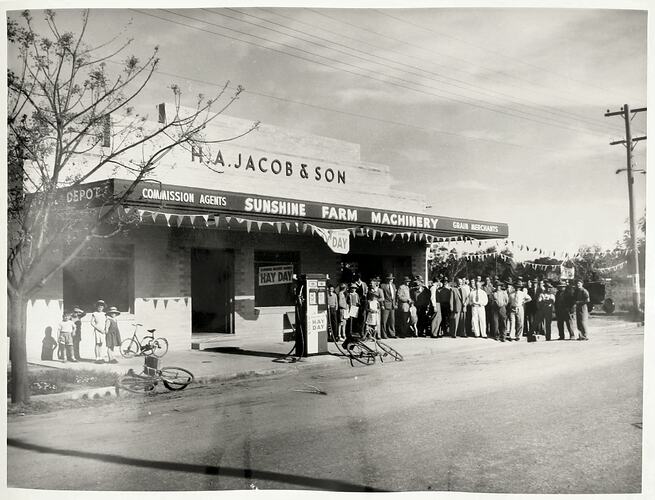 Crowd of people outside agricultural machinary shop.