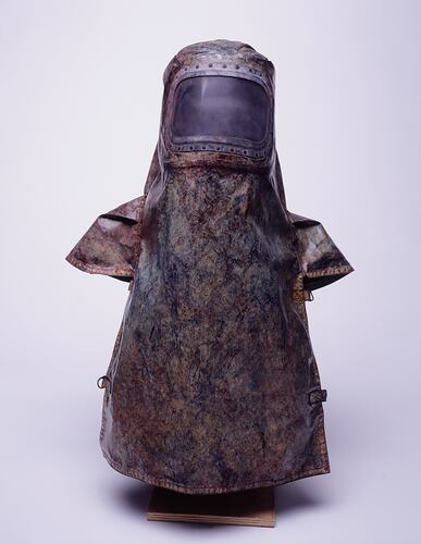 Discloured brown safety hood and apron. Discoloured clear plastic section over face. Capped shoulders.