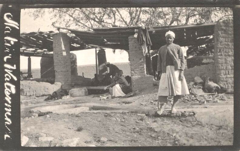 Man in front of mud brick shelter.
