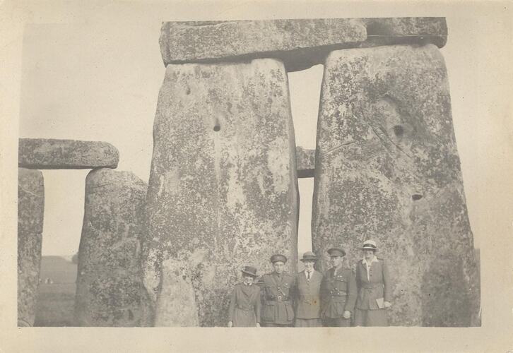 Three woman and two men in military uniforms standing in front of stone monument.