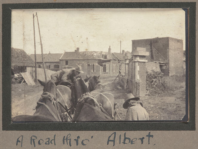 Two men with horses, on street with damaged houses on both sides of road.