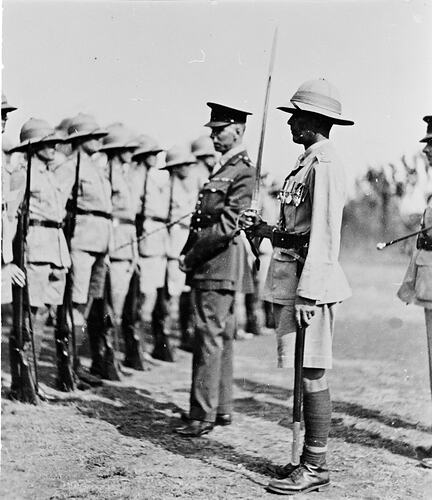 Three servicemen, one holding sword, facing row of soldiers.