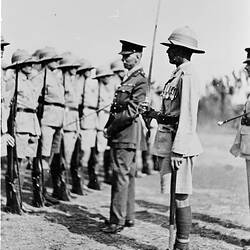 Three servicemen, one holding sword, facing row of soldiers.