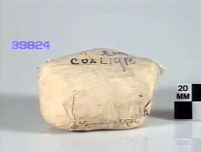 Rectangular piece of coal sewn up in white linen marked 'Coal May 1918'.