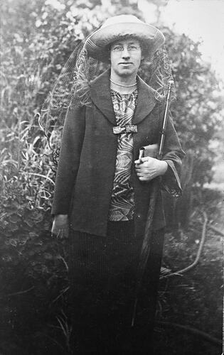 Woman posing wearing dark veiled hat and holding book.