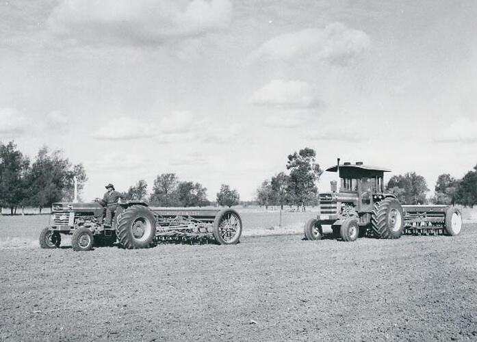 2 tractors pulling seed drills, in a prepared field.