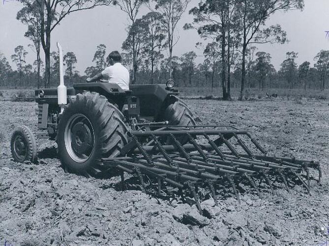 Rear end view of a man driving a tractor with a tiller.