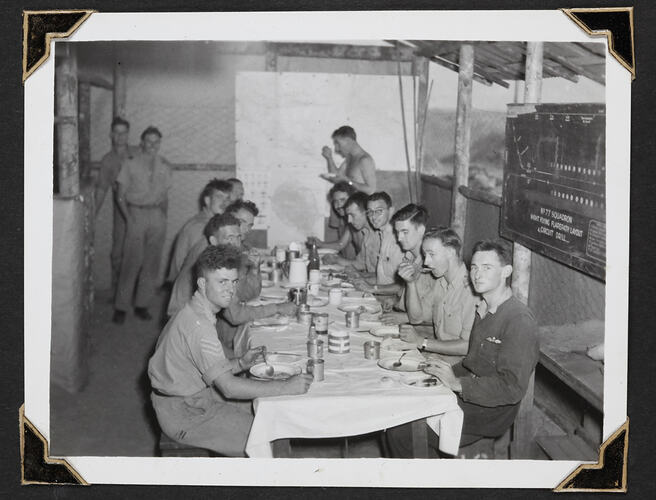 Eleven men sitting around long table eating, three men behind standing.
