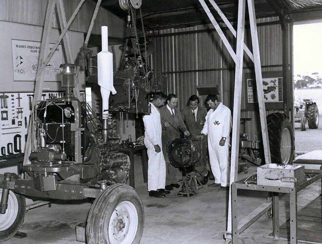 Four men standing by a tractor in a workshop.
