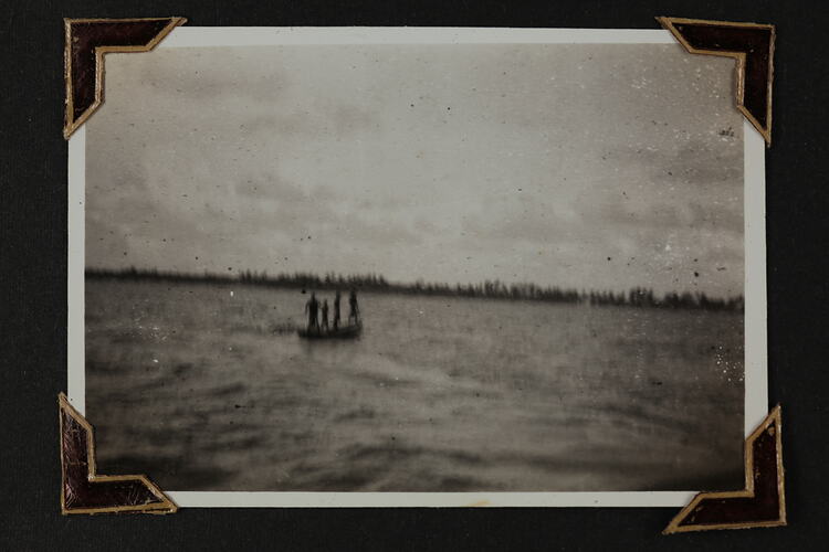 Four people standing on a small boat, with land in distant background.