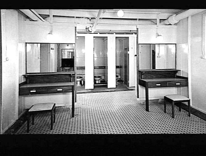 Ship interior. Tiled women's toilets. Three cubicle stalls in centre, table with mirror on either side.