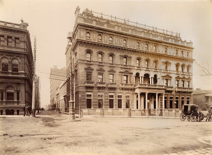 Four storey stone building, large balcony on second level. Horsedrawn vehicles out front.