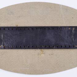 Oval shaped card with strip of film stapled to front.