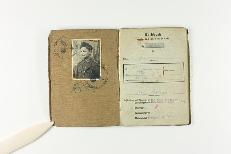 Open book page with photograph of soldier and two stamp marks on right page, printed and written text on left.