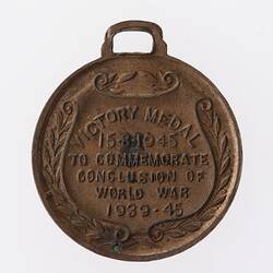 Round bronze medal with text on shield-shaped scroll framed by wreath. Loop at top.