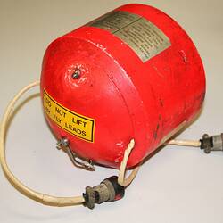 Bright orange-red metal cylindrical casing with domed ends, plates and labels. Two cords fixed at ends.