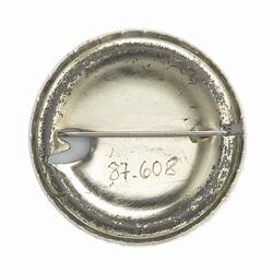 Back of round silver metal badge with horizontal pin.