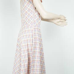 Knee length sleeveless dress with white, yellow, blue and red checked pattern, side view.