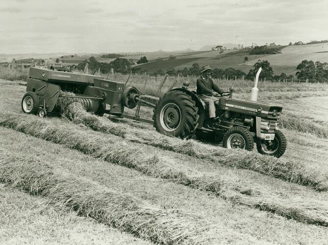 Man driving a tractor fitted with a Pick Up Hay Baler picking up neat windrows of hay.