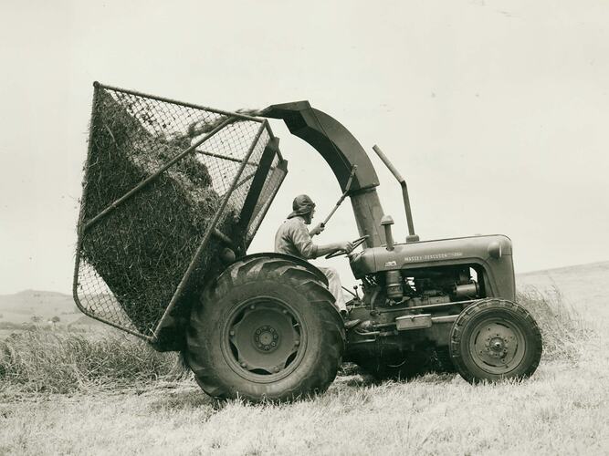 Man driving a tractor fited with a forage harvester. Storage cage being filled.