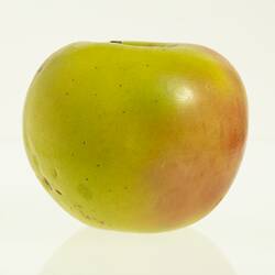 Wax model of an apple with stem, painted yellow with some red tinge.