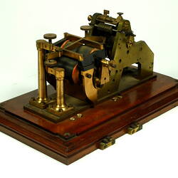 Brass apparatus on wooden base, three quarter view.