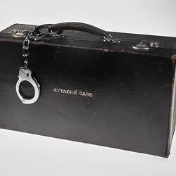 Black leather briefcase marked 'Attache Case' with handcuffs on the handle.