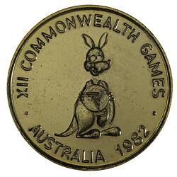 Round gilt medal with kangaroo caricature standing facing 3/4 right holding Brisbane Commonwealth Games logo.