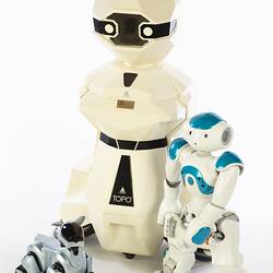 Cream plastic robot with angular human-like shape, ie. head, shoulders, waist and legs. Siver robot dog at left, smaller blue white root at right.