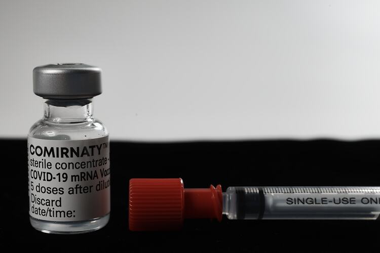Glass vial with white printed label and metal cap beside syringe with black text and red cap.