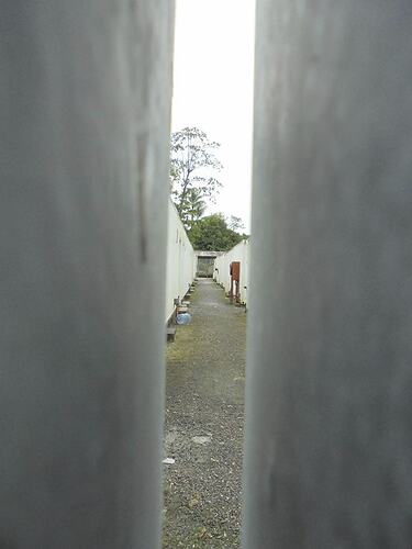 View through narrow opening of a gravel footpath, building walls either side.