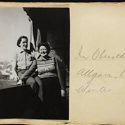 Black and white photo on off-white page. Handwritten text in pencil. Features two women posing on balcony.