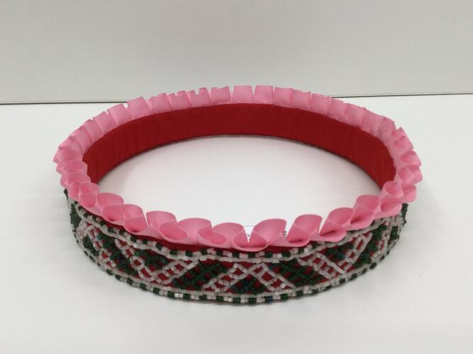 Round beaded crown with pink ruffled ribbon trim around the top. Green and white plastic beads.