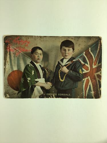 Two children shaking hands, facing front. Left holds Japanese flag, right holds English flag.