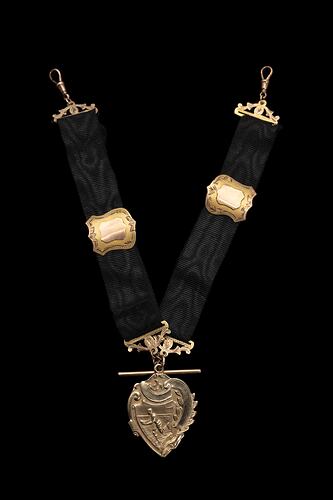 Gold fob with two black ribbed straps, each with a central gold shield-shaped slide and gold clips at top ends. The decorative heart-shaped fob is engraved with a running footballer holding a football.