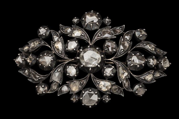Silver oval brooch with gold base. Cutaway leaf motif design. Central diamond with 44 smaller diamonds around.