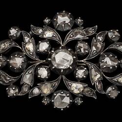 Silver oval brooch with gold base. Cutaway leaf motif design. Central diamond with 44 smaller diamonds around.