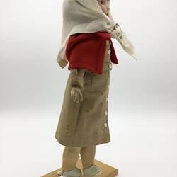 A doll dressed as a nurse in a brown dress, red capelet and white scarf