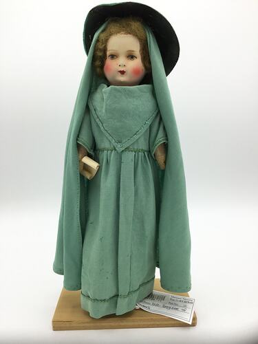 A doll dressed in a long green gown, veil and hat
