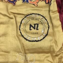 Detail of embroidered lettering and a stamp on cream lining of multicoloured patchwork skirt.