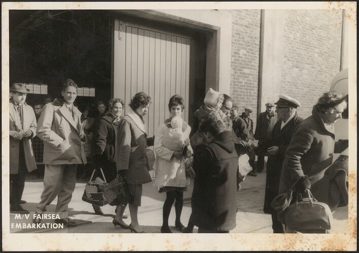 Passengers wearing coats and hats lining up to board a ship.