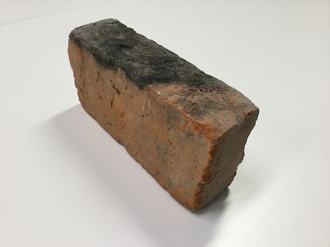 Red clay brick with one blackened edge.