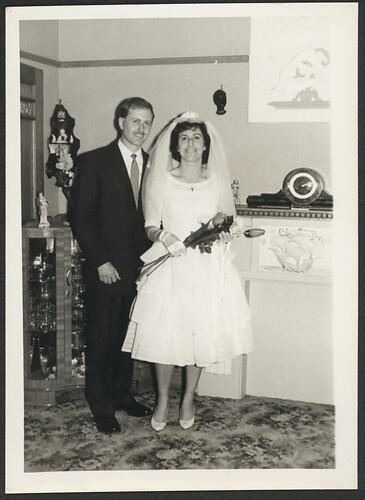 Groom and bride posing indoors in front of fireplace mantel.