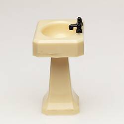 Toy bathroom sink made of cream coloured moulded plastic. Two faucets. Profile.