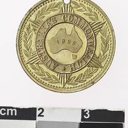 Round gold coloured medal with Australia in centre, surrounded by text, with wreath surrounding.